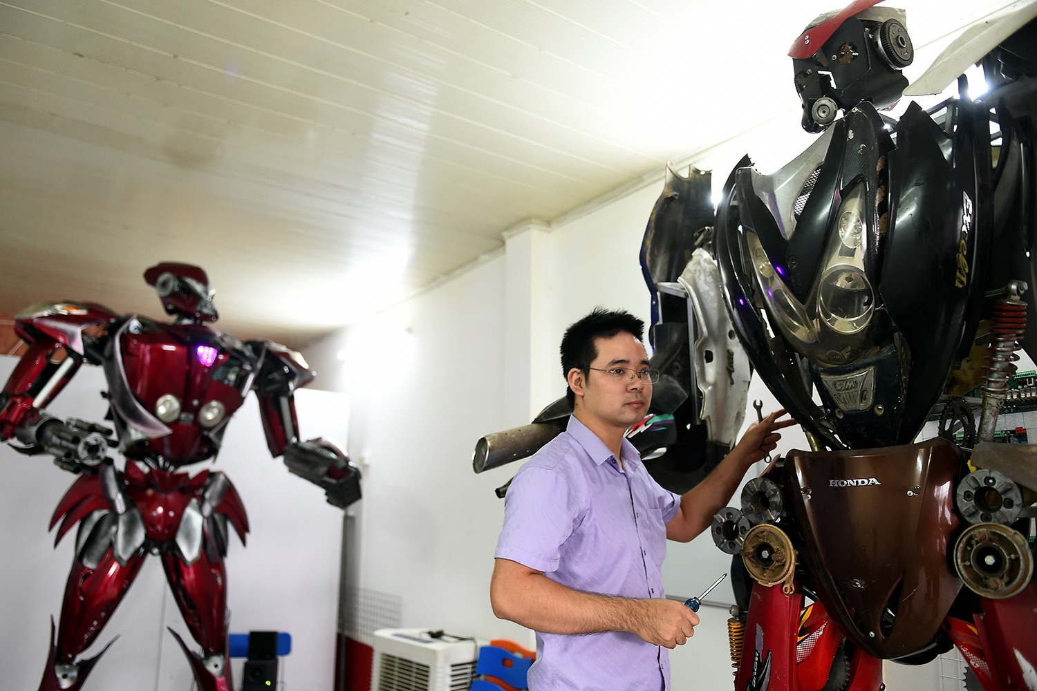 A new robot-model next to “Robot-One”, made from spare motorcycle parts, at a workshop in Hanoi.A new robot-model next to “Robot-One”, made from spare motorcycle parts, at a workshop in Hanoi.
