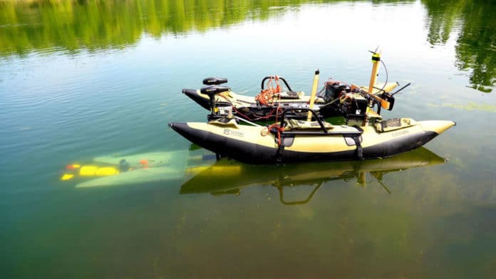 A yellow underwater robot (left) finds its way to a mobile docking station to recharge and upload data before continuing a task.