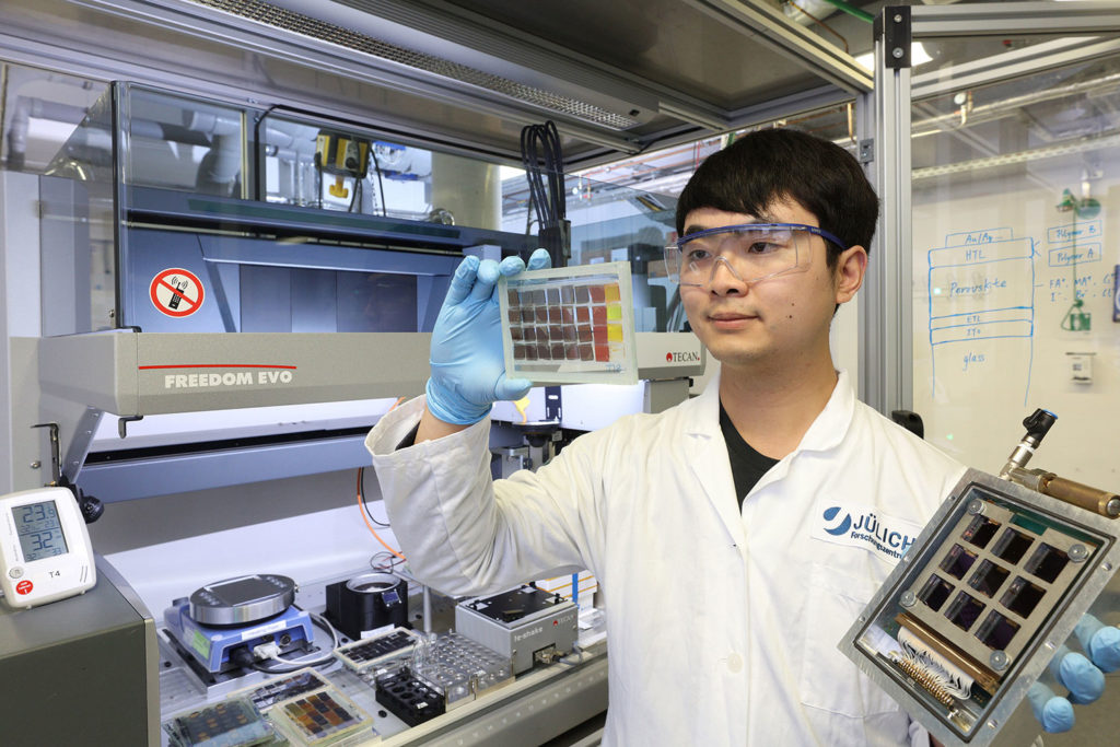 Dr. Yicheng Zhao in front of High Throughput Research Equipment holding Perovskite Solar cell and film samples.