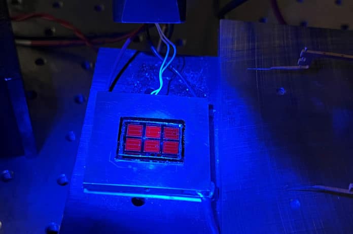 The record-setting solar cell shines red under blue luminescence.
