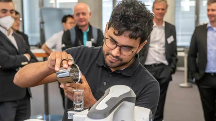 Dr. Luis Figueredo demonstrates how a robotic arm transports a glass filled with water.