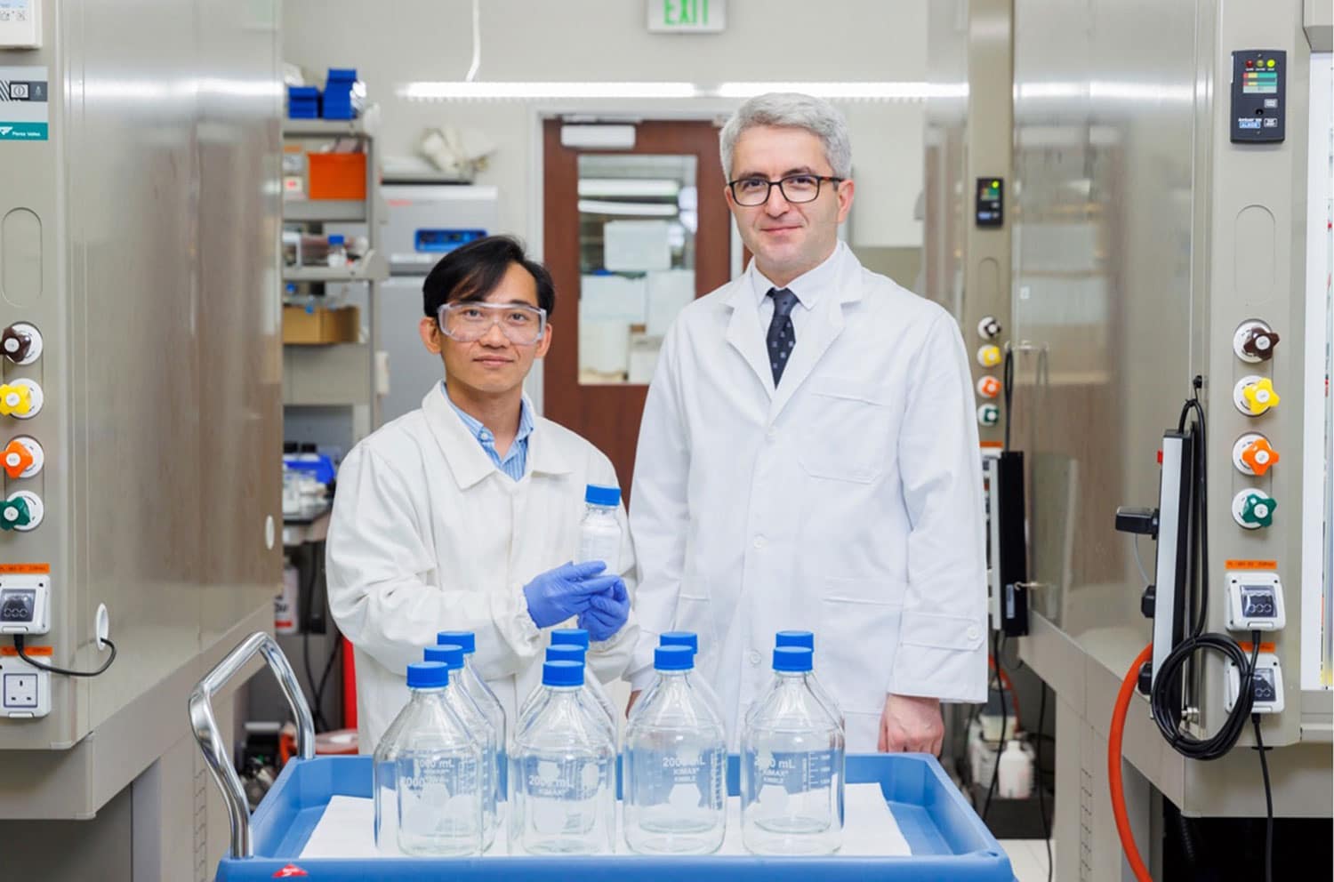 Dr. Thien Nguyen (left) and Professor Cafer T. Yavuz (right) pose with a bottle of CO2-loaded guanidinium sulfate salt (held by Dr. Nguyen). The ten gas-filled, two-liter bottles in front represent the required space for the same amount of carbon dioxide that would be needed were it not being held in clathrate form (small bottle).