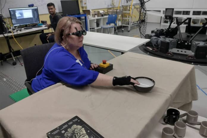 A research team member who is blind uses acoustic touch to locate and reach for an item on the table.