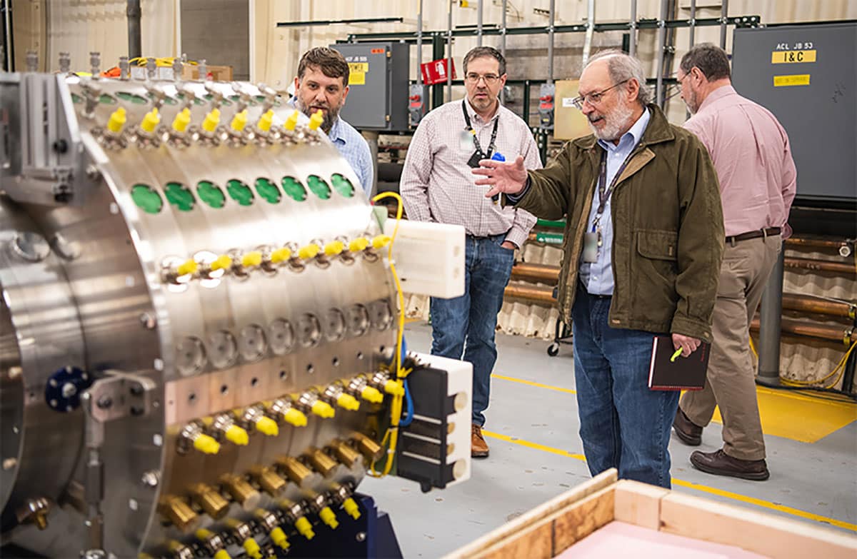 Bob Webster, deputy Laboratory director for Weapons (far right); Mike Furlanetto, Scorpius Advanced Sources and Detection project director (center); and Geoffrey Zehnder, project engineer (far left); discuss the prototype module Lab employees constructed for Scorpius' first accelerator cells and modules.